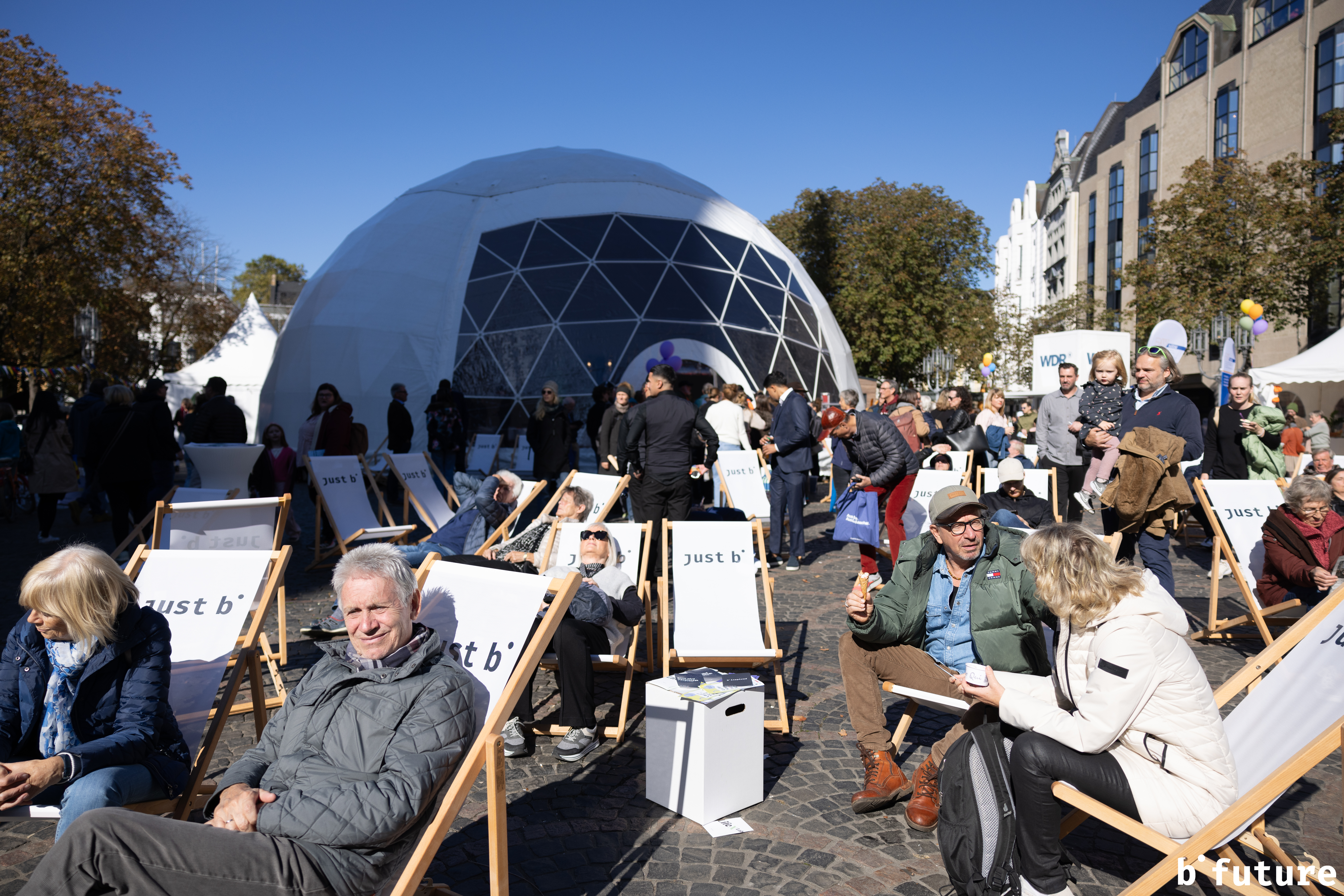 Menschen sitzen in Liegestühlen auf dem Münsterplatz, im Hintergrund steht das große Kuppelzelt (Lila Zelt).