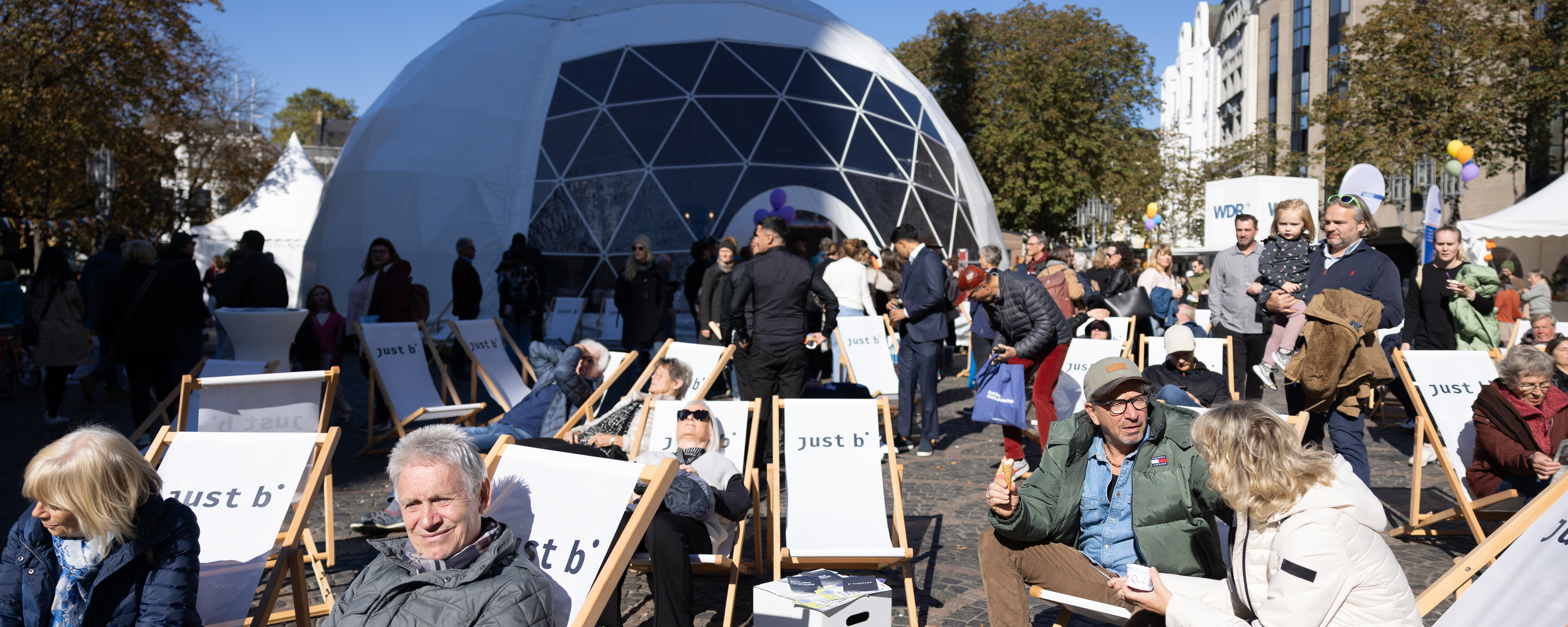 Menschen sitzen in Liegestühlen auf dem Münsterplatz, im Hintergrund steht das große Kuppelzelt (Lila Zelt).