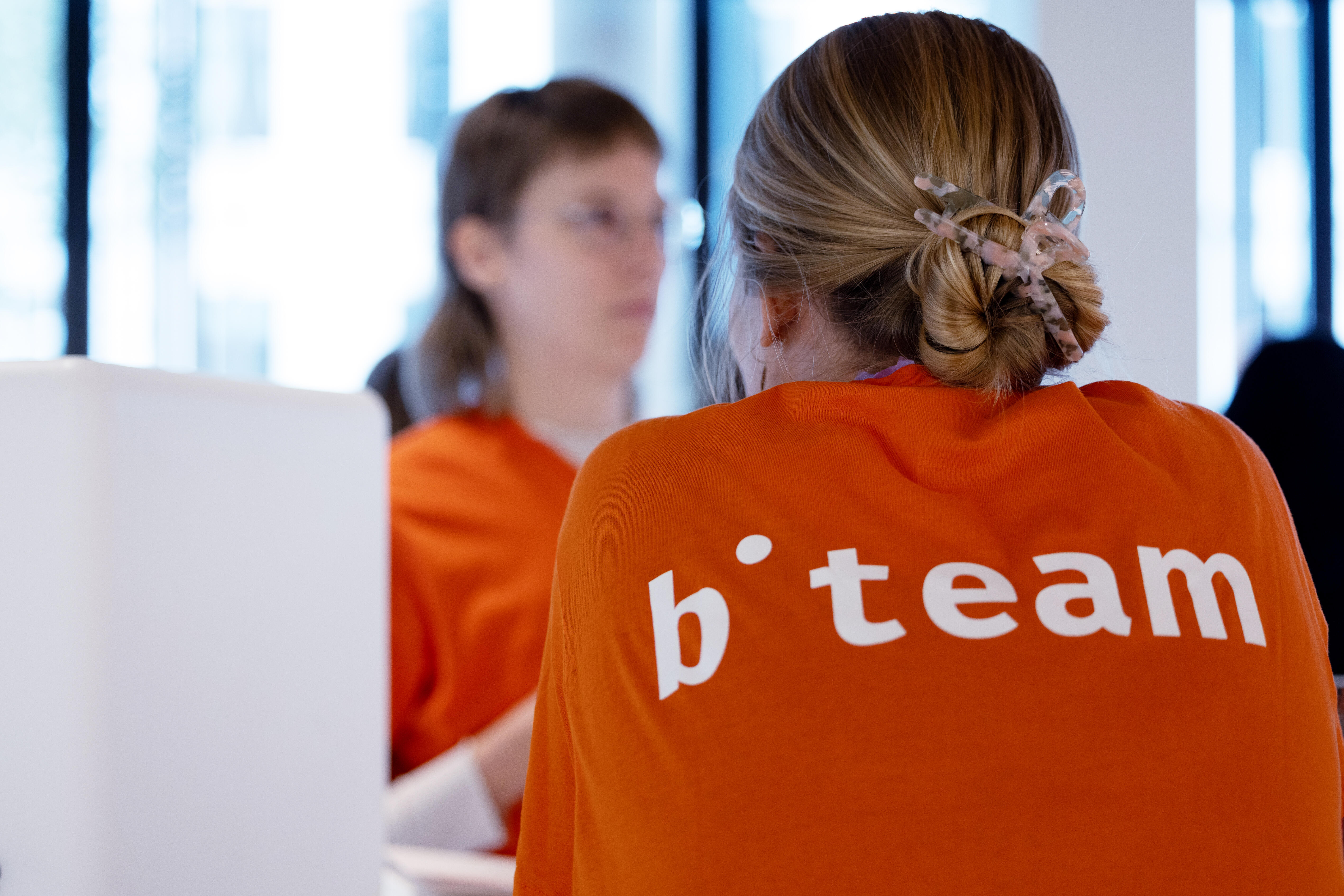 One Team member of the b° team wearing an orange shirt turned with her back to the camera